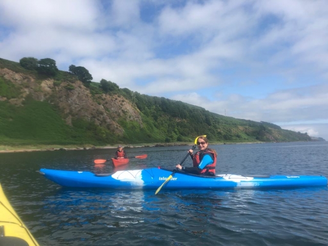  Mujer con lentes de sol y ayudas de flotabilidad rojas, sonriendo y kayak en kayak azul